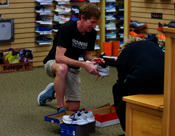 male store salesperson checking the fit of running shoes on a customer's right foot